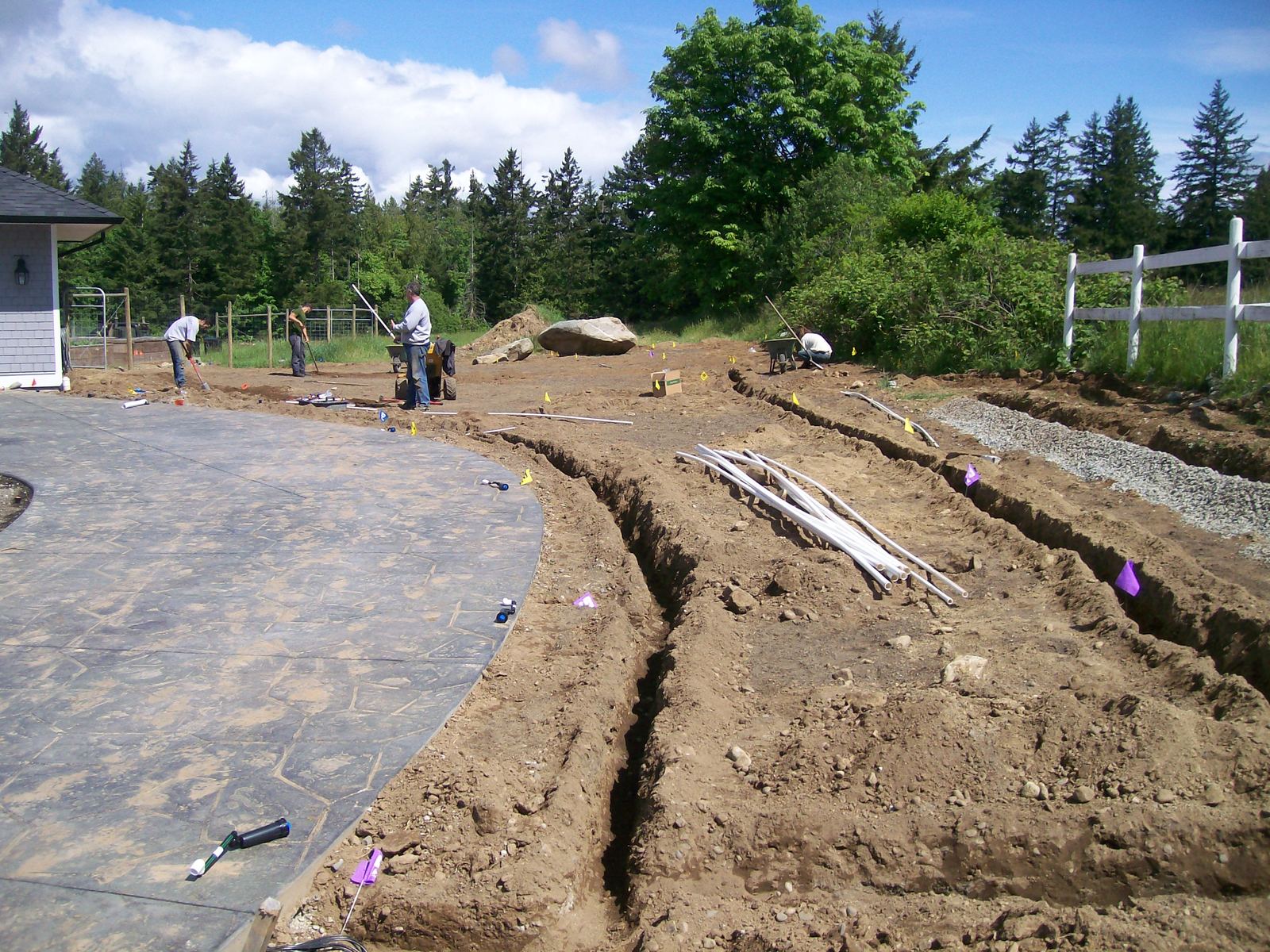 Irrigation installation trenching pvc pipe victoria Irrigation crew laying PVC pipe in open trenches beside a new stamped concrete driveway in Victoria, BC